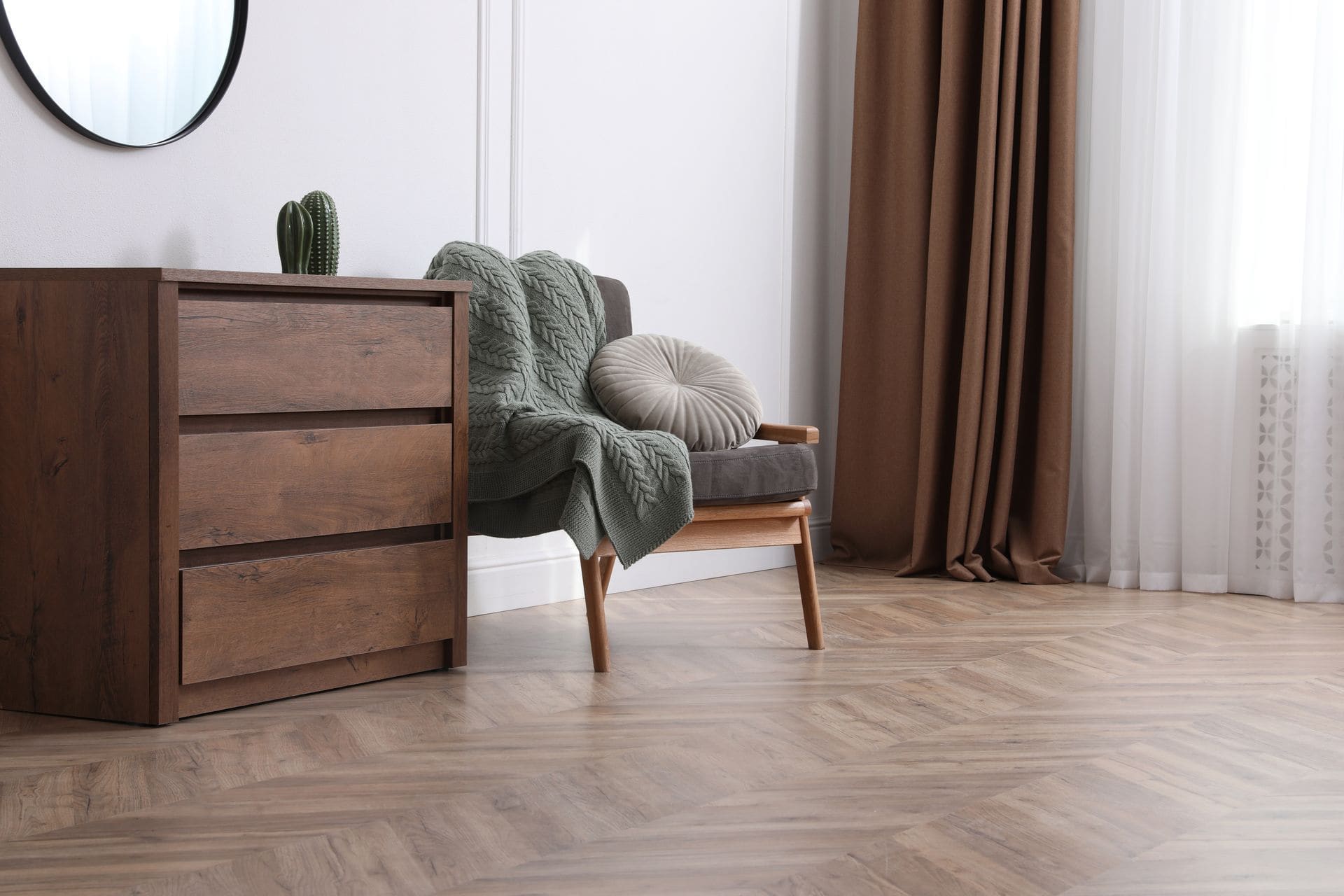 Modern bedroom with wooden dresser, gray armchair, green throw blanket, and beige round pillow