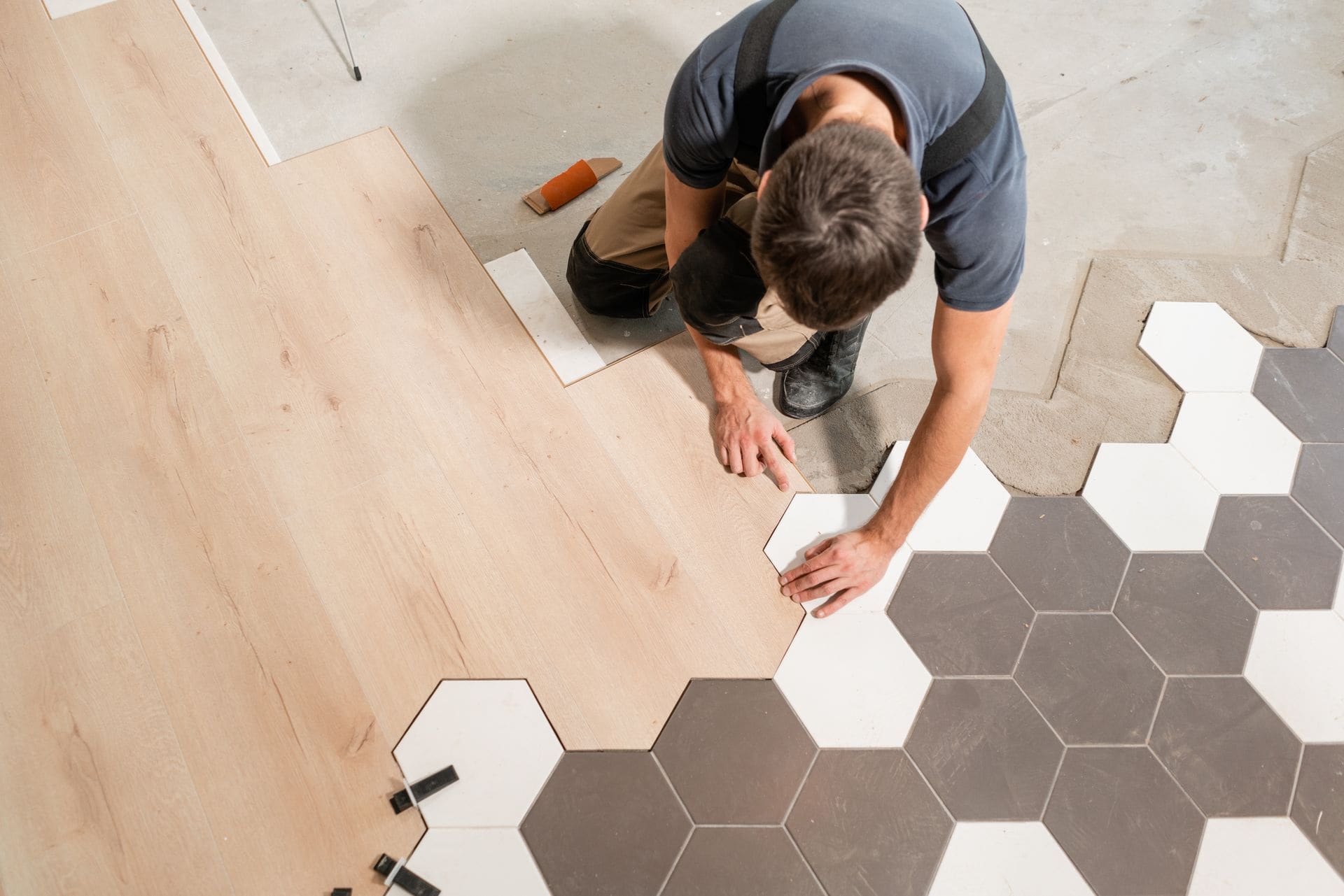 Worker installing hexagonal floor tiles in alternating white and gray pattern