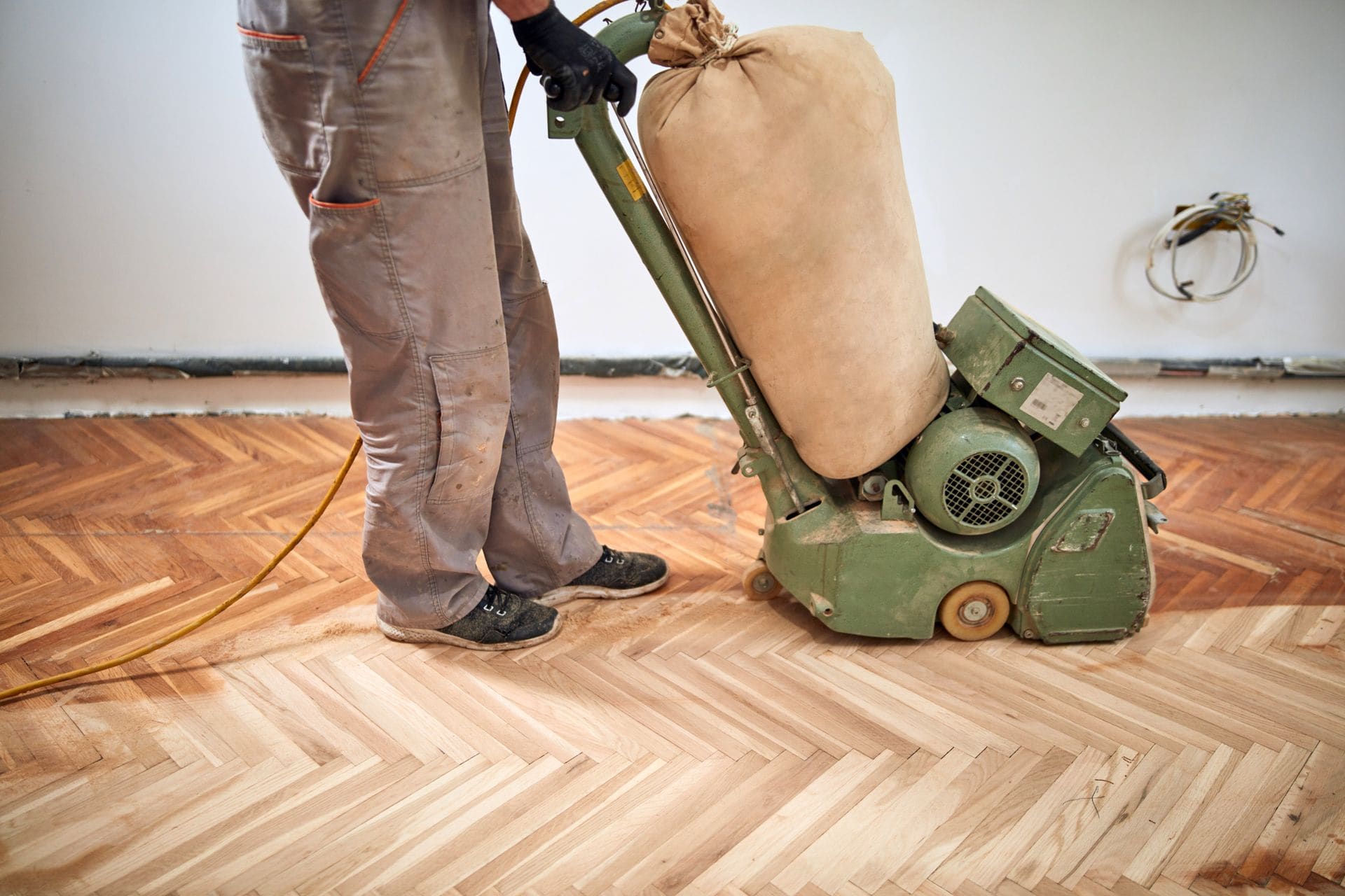 Worker operating green floor sanding machine on parquet flooring