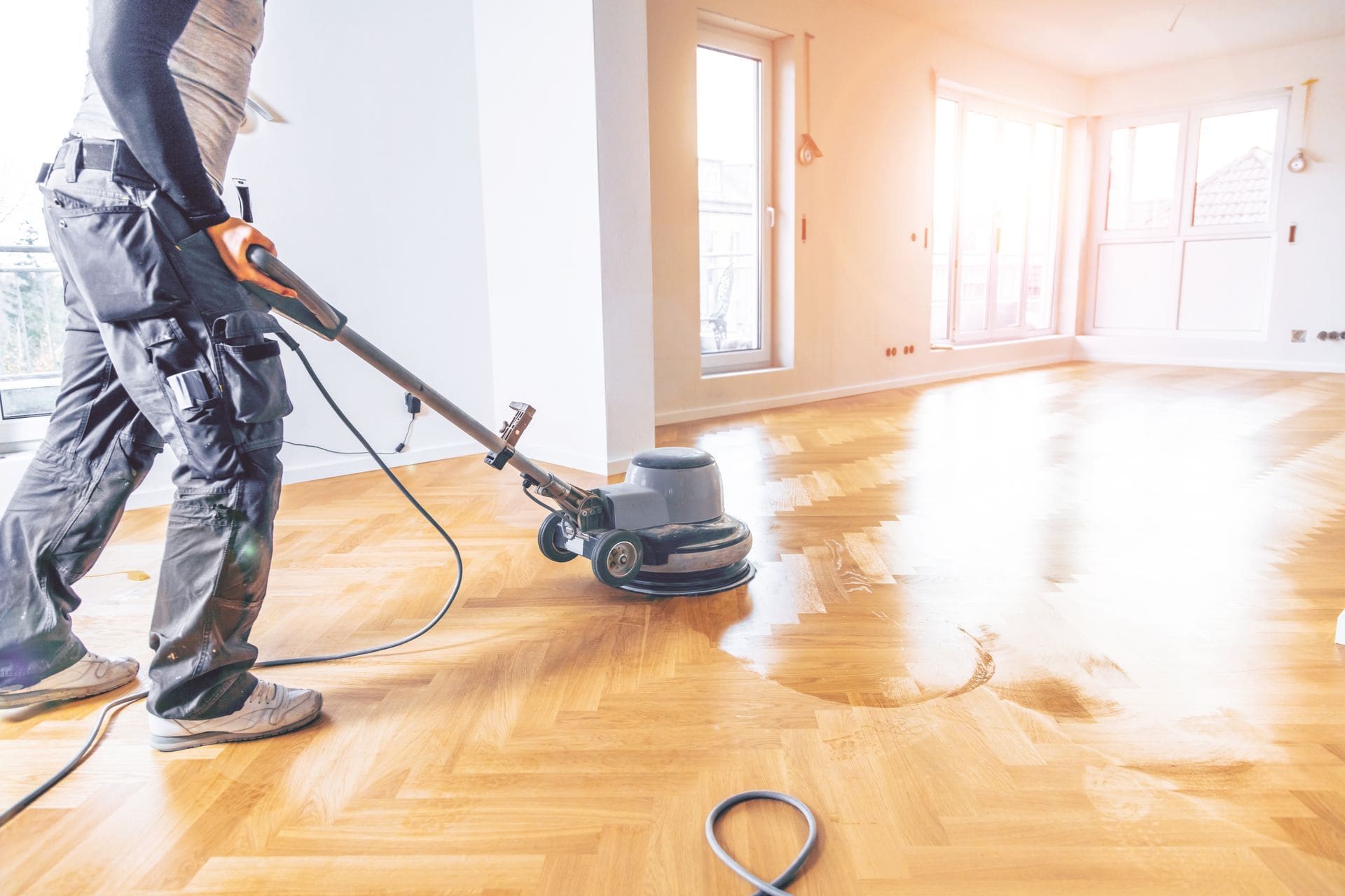 Professional floor polisher operating a rotary machine on wooden parquet flooring in an empty residential room